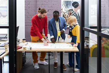 Canvas Print - Group of architects standing at table and working over blueprint in team, they discussing new construction project