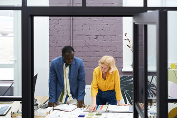 Poster - Mature businesswoman discussing colours with her colleague designer while they standing at table with colour palette