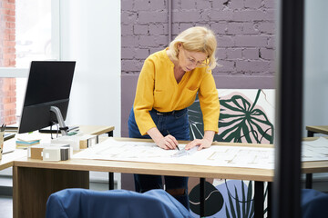 Poster - Female construction engineer working at office desk, she drawing on a building project with a pencil and a ruler