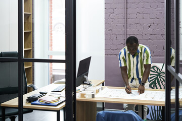 Poster - African construction engineer drawing blueprint at table with pencil and ruler, he working over project at office