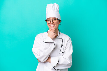 Wall Mural - Young caucasian chef woman isolated on blue background with glasses and smiling