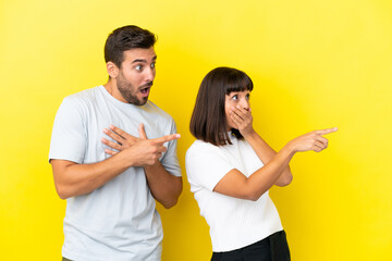 Wall Mural - Young couple isolated on yellow background pointing finger to the side with a surprised face