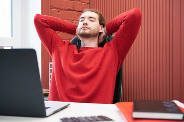 Poster - Young businessman sitting on chair and strestching, he relaxing at his workpace with laptop after hard work at office
