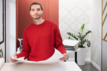 Poster - Portrait of young designer looking at camera while working with sketches at office