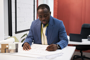 Poster - African male designer concentrating on his work at table, he drawing blueprint of apartment plan