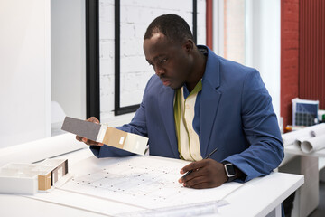 Poster - Serious African architect looking at samples and drawing plan of new building at table