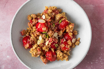 Wall Mural - Delicious strawberry crumble with oats, almonds and pumpkin seeds in a plate on pink background. Close up