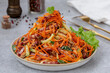 Grated marinated carrot salad with salami, cucumber and croutons, tossed together in a homemade dressing. Selective focus, gray concrete background. Horizontal