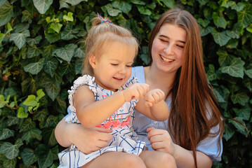 Joyful older sister holding younger sister, playing and laughing, having fun. Teen girl holding baby girl on summer day. Children with large age gap. Big age difference between siblings