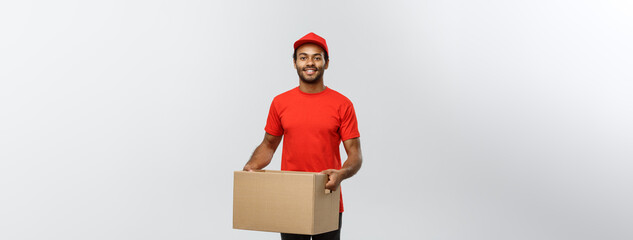 Poster - Delivery Concept - Portrait of Happy African American delivery man in red cloth holding a box package. Isolated on Grey studio Background. Copy Space.