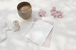 Wedding composition. Feminine spring breakfast still life. Pink Japanese cherry tree, sakura blossoms in sunlight. Blank greeting card, invitation. Cup of coffee. White dappled table background.