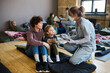 © pressmaster - Young female refugee and her little son consulting with healthcare worker in uniform, gloves and protective mask while sitting on sleeping place