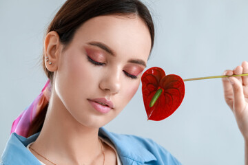 Wall Mural - Beautiful woman with closed eyes holding anthurium flower on light background