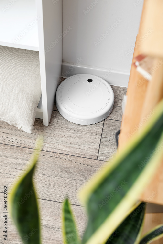Modern robot vacuum cleaner on wooden floor near light wall