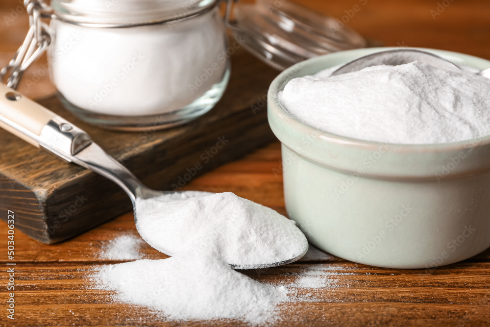 Bowl and spoon with baking soda on wooden background, closeup