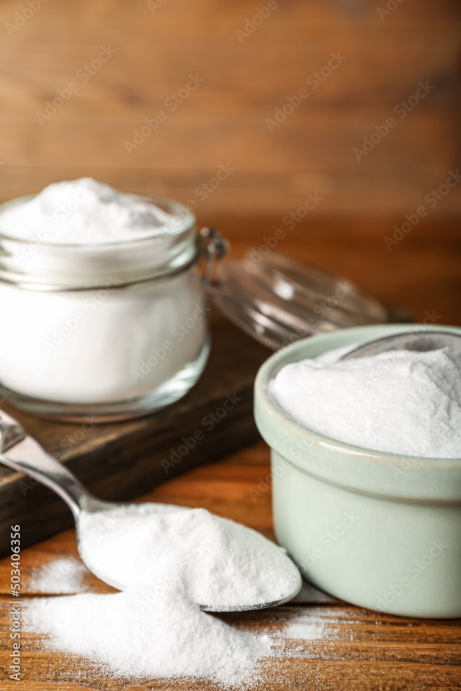 Spoon and bowl with baking soda on wooden background, closeup