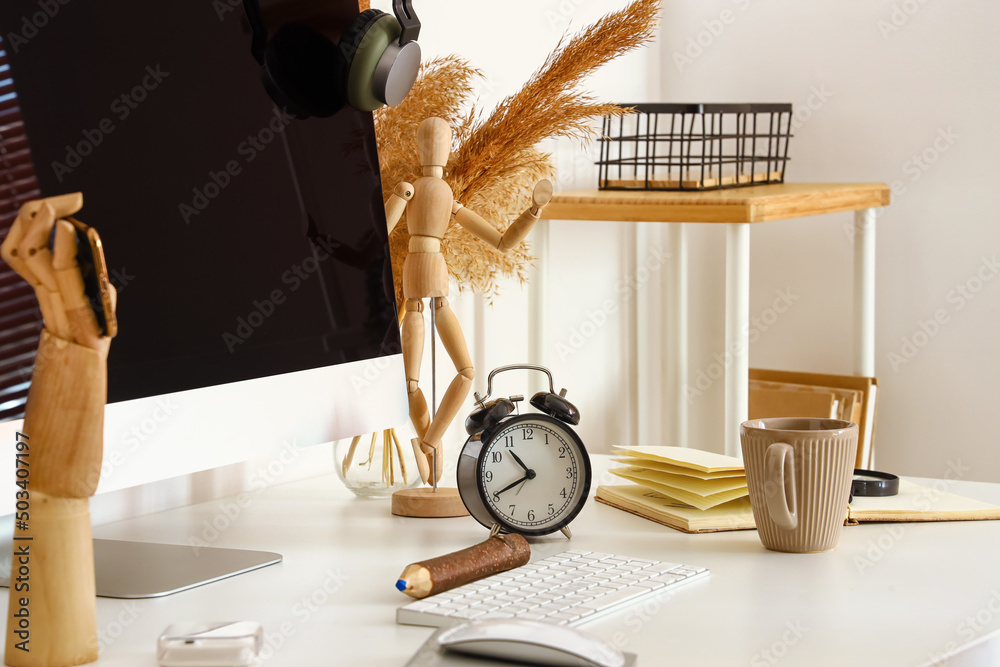 Modern computer, alarm clock and stylish decor on table near light wall, closeup
