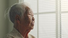 Lonely Old Senior Asian Woman, Sitting Alone In The Room, Looking Through The Window