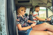 © David Pereiras - Couple traveling in camper van. Man driving and woman looking at mobile