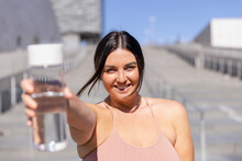 Smiling Woman Showing Water Bottle Standing In Front Of Stairs