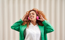 Smiling Businesswoman With Eyes Closed Listening Music Through Wireless Headphones In Front Of Wall