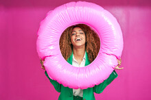 Happy Young Businesswoman Looking Though Inflatable Ring Against Pink Background