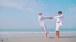 © ronnarong - Asian retired couple relaxing by the sea in summer. A senior woman dancing with her partner on the beach.