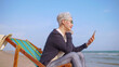Asian elderly woman chatting with friends on video call while relaxing at the beach