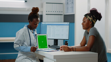 Wall Mural - Medic pointing at tablet with green screen and talking to patient for consultation. Doctor and woman with technology looking at chroma key with isolated background and mockup template