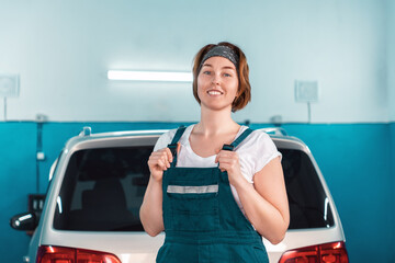 Wall Mural - Portrait of a young caucasian smiling plus-sized woman in overall. At the background a car in an auto repair shop. The concept of women's equality