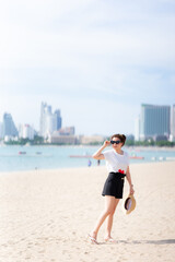 Wall Mural - Teenage girl standing on beach looking at beautiful scenery, holding straw hat and sunglasses, smiling brightly. During summer or spring. On comfortable travel day. Empty space. Vertical image.