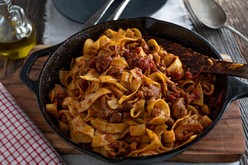 Wall Mural - Braised chicken meat with tomato herb sauce and pasta in a rustic cast iron pan