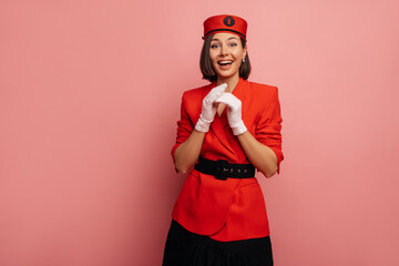 Sticker - Happy young caucasian brunette girl is pleasantly surprised with mouth open while standing on pink background. Beauty model wears stylish red jacket. Elegant, fashion trend concept