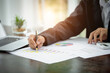 © Tinnakorn - Business man work on statistics and business graphs, Businessman holding a pen is working with graph documents, Stock market chart.