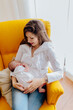 Young mother breastfeeding her newborn baby boy sitting on yellow armchair