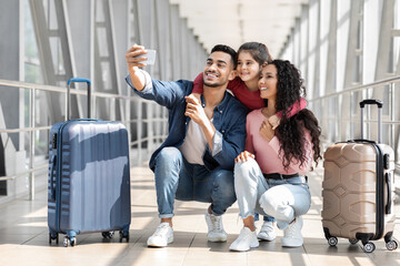 Wall Mural - Joyful Middle Eastern Family Of Three Taking Selfie With Smartphone In Airport