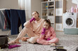 © ABCreative - Housewife sitting on the floor with her daughter, supporting herself under chin with a rubber glove, resting women after work. Exhausted girls tired after housework, prepared for Christmas.