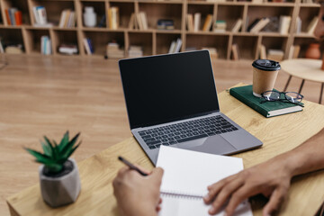 Poster - Online class concept. Male student writing in notebook, taking notes and using laptop with black screen for mockup