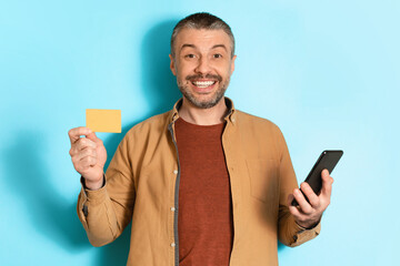Poster - Middle Aged Man Holding Cellphone Showing Credit Card, Blue Background