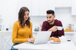 © LIGHTFIELD STUDIOS - Smiling woman using laptop near muslim man and breakfast in kitchen.
