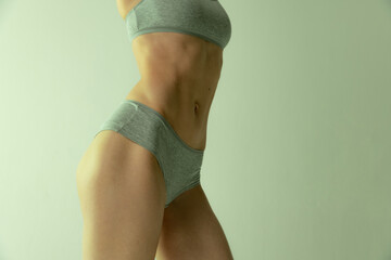 Wall Mural - Cropped image of slim muscular female body in cotton underwear isolated over grey studio background. Fit body