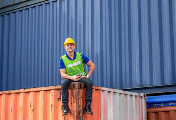 Worker with walkie talkie sitting on container box relaxing at cargo containers, Portrait of cheerful engineer man in hard hat and safety vest