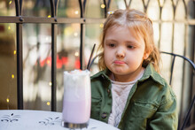 Girl Pouting Lips While Looking At Blurred Milkshake In Street Cafe.