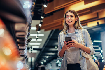 Wall Mural - Young woman in grocery using phone