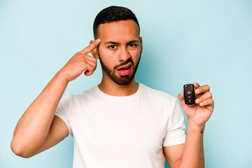 Wall Mural - Young hispanic man holding car keys isolated on blue background showing a disappointment gesture with forefinger.