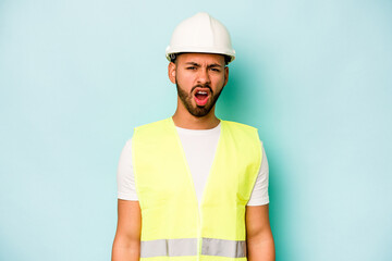 Wall Mural - Young laborer hispanic man isolated on blue background screaming very angry and aggressive.