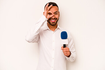 Wall Mural - Young hispanic TV presenter isolated on blue background excited keeping ok gesture on eye.