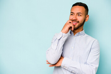 Wall Mural - Young hispanic man isolated on blue background relaxed thinking about something looking at a copy space.