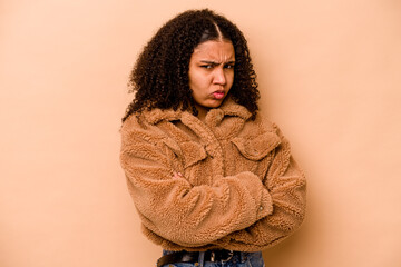 Young African American woman isolated on beige background frowning face in displeasure, keeps arms folded.