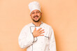 © Asier - Hispanic chef man isolated on beige background laughs out loudly keeping hand on chest.